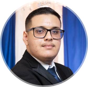 Ariel usando óculos com terno preto e gravata azul escuro, olhando pra câmera